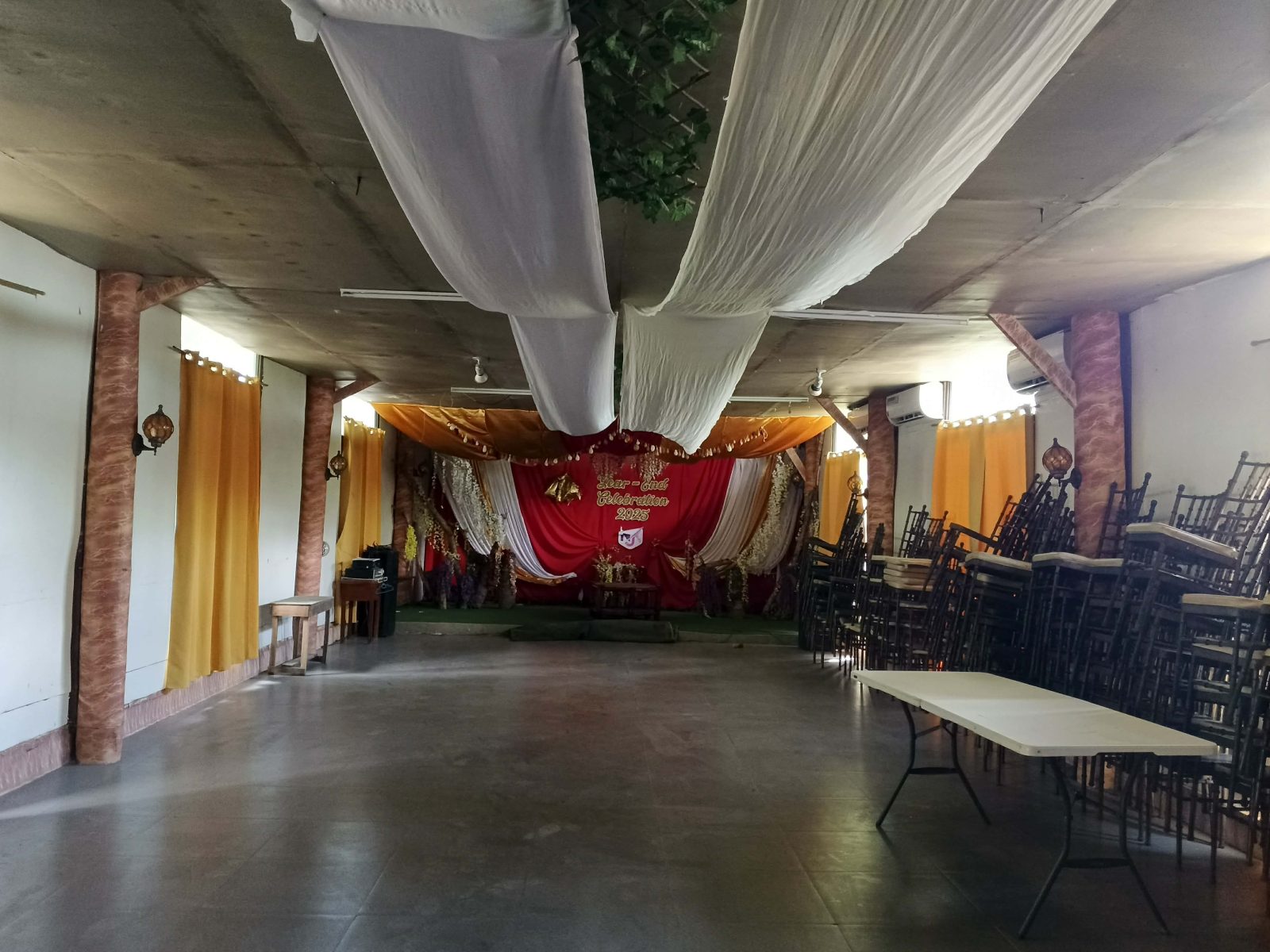 The function hall with draped ceiling, stage backdrop, and stacked chairs